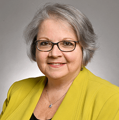 grey haired smiling woman with a yellow jacket